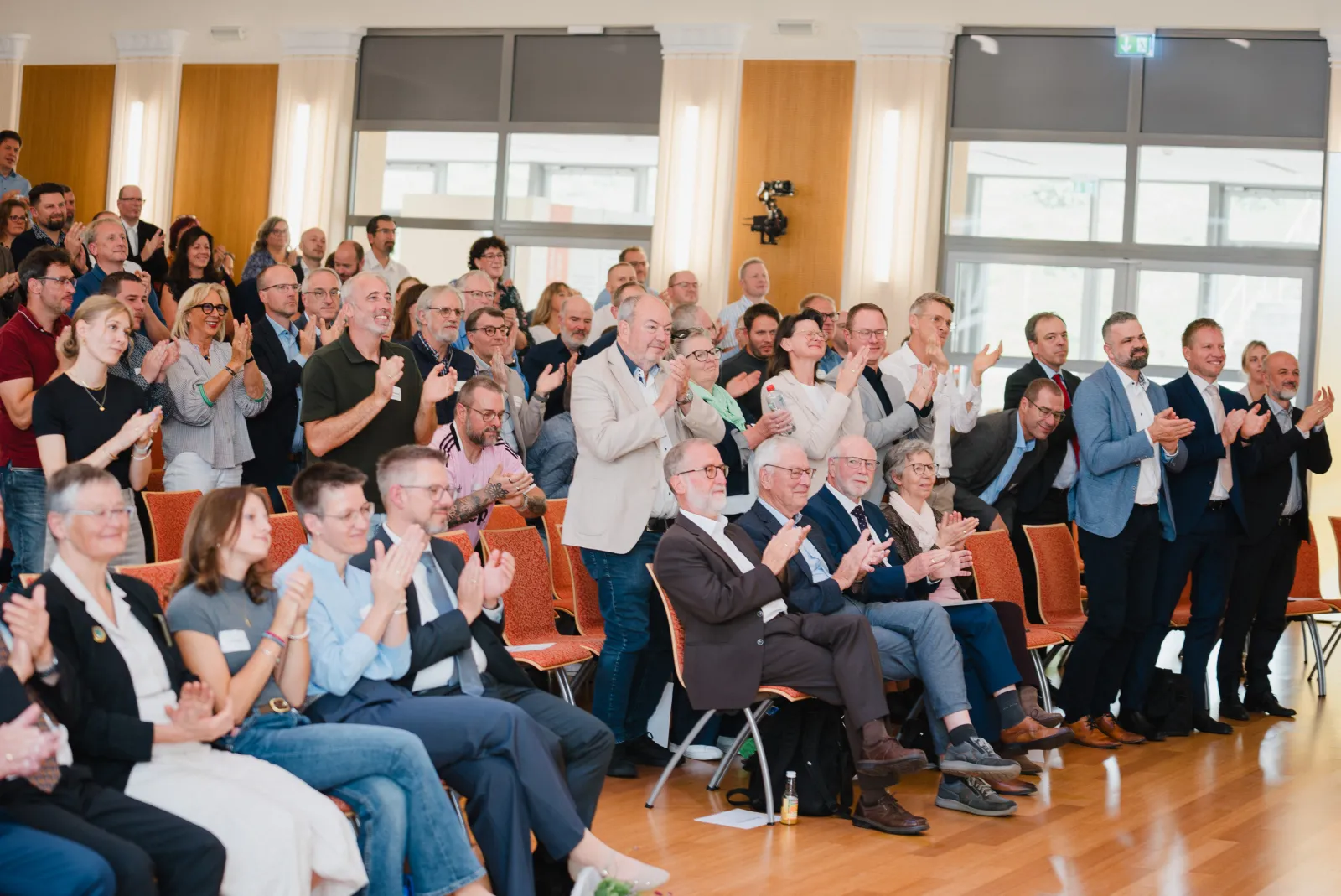 Gäste im Saal applaudieren, einige stehen