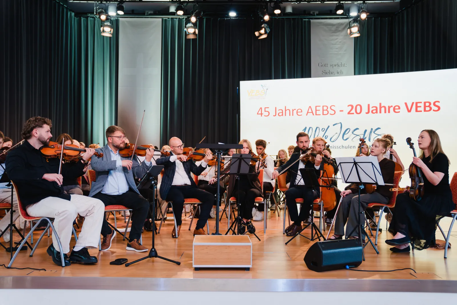 Streicherinnen und Streicher des Orchesters auf der Bühne vor dem Banner 45 Jahre AEBS – 20 Jahre VEBS